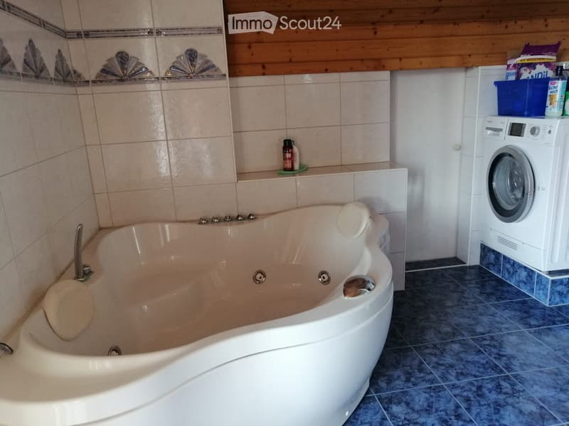 Bathroom with a large bathtub, washing machine, and shelves holding various items.