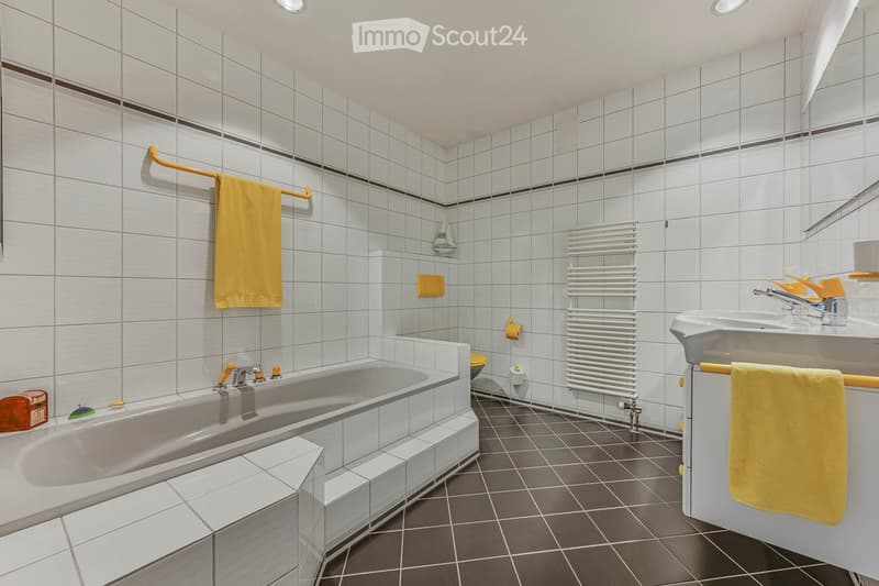 Modern bathroom with white tiled walls and dark tiled floor, featuring a bathtub, sink, radiator, and towels.