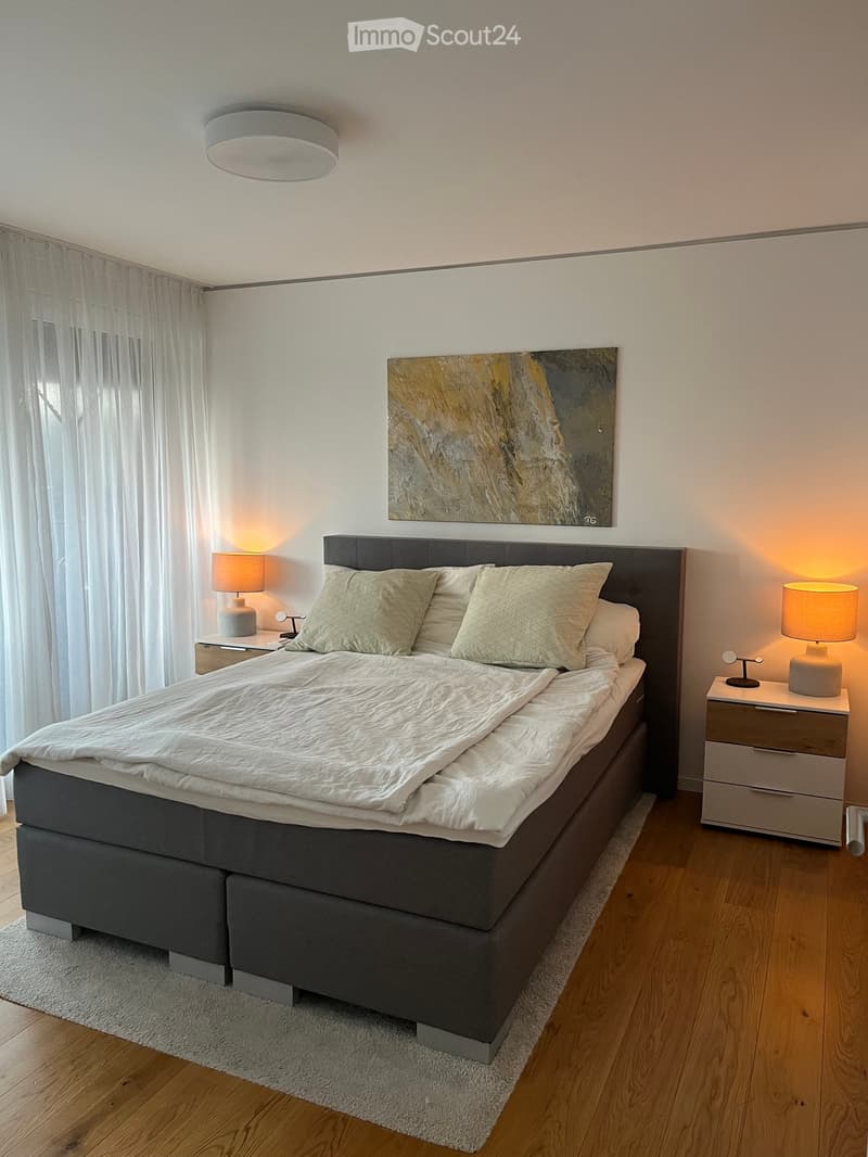 Modern bedroom with a large bed, nightstands, lamps, and a painting on the wall.