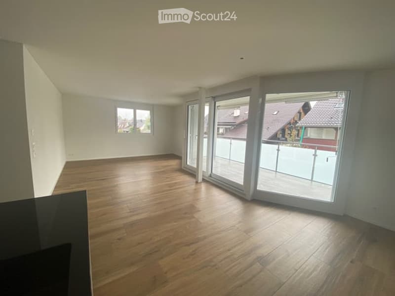 Empty room with wooden flooring, large sliding glass doors leading to a balcony, and a small window on the opposite wall.