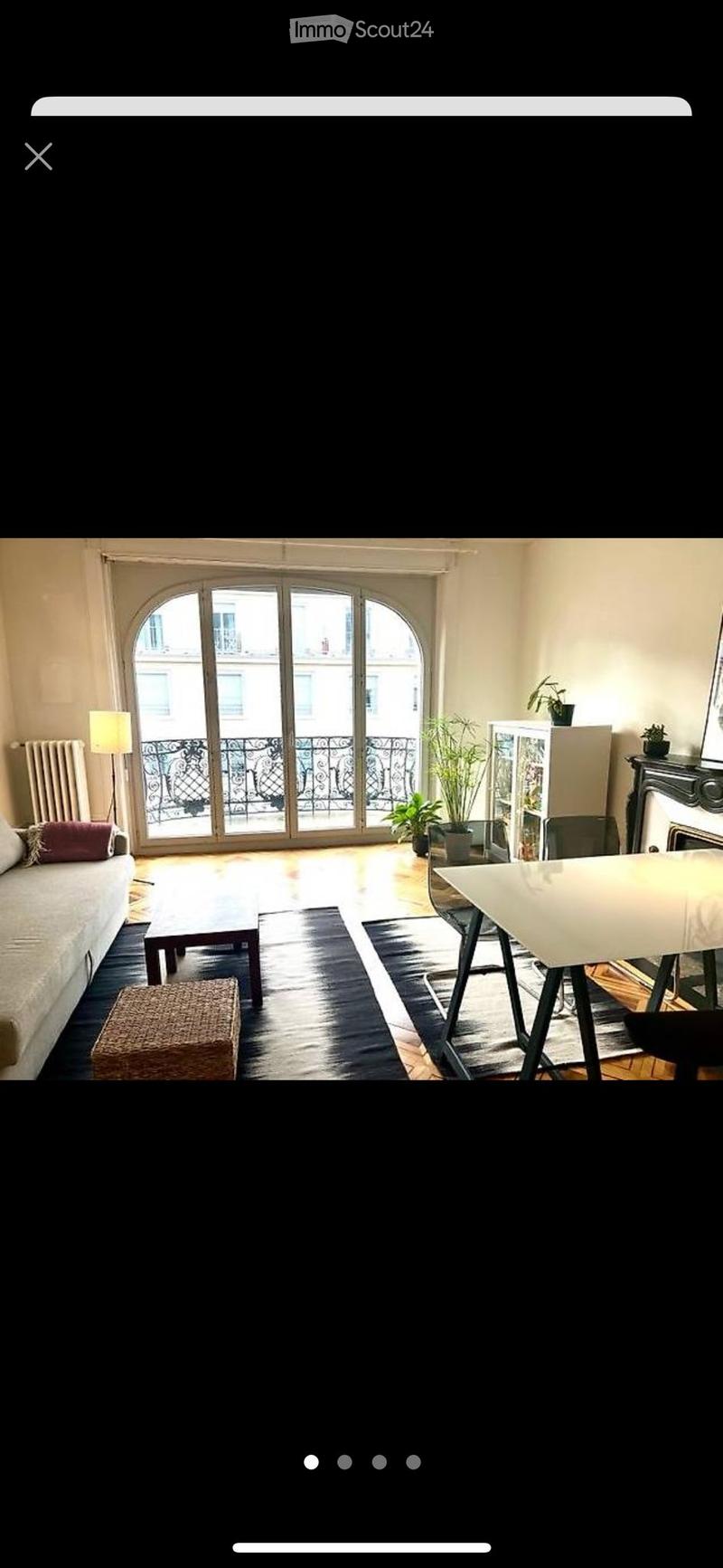 Bright living room with large arched windows leading to a balcony, featuring a sofa, coffee table, dining area, and decorative plants.