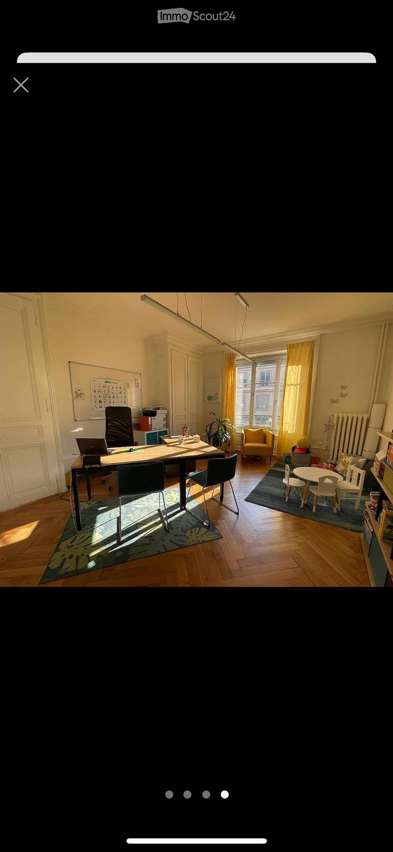 Bright, multi-functional room with wooden flooring, large windows, a desk area with a laptop, a small seating area with a sofa, and a children's play area with a small table and chairs.