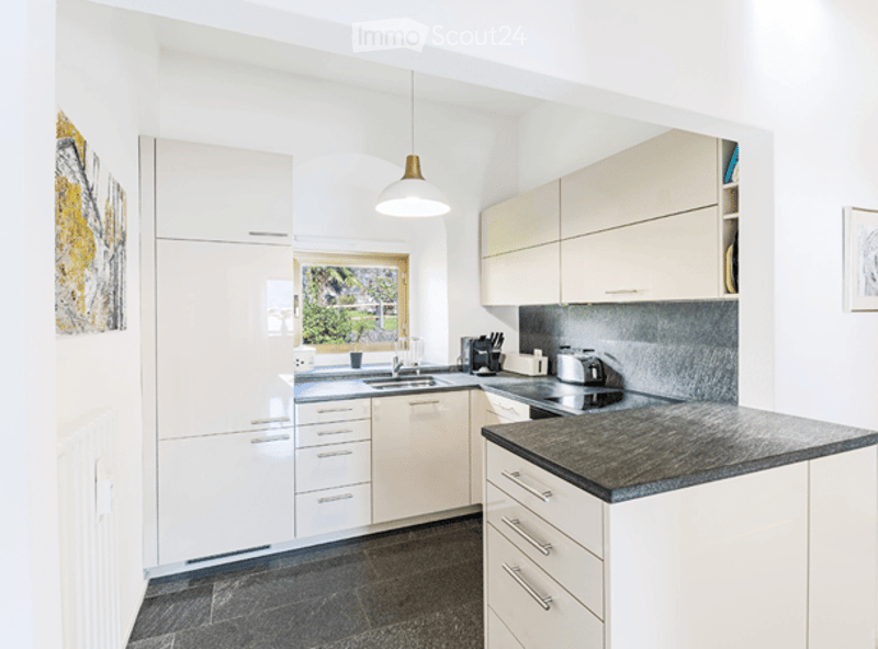 Modern kitchen with white cabinets, granite countertop, stainless steel appliances, and a view through a window.