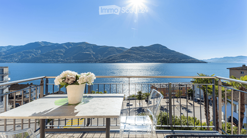 Balcony with a table and vase of flowers, overlooking a scenic lake and mountain view.