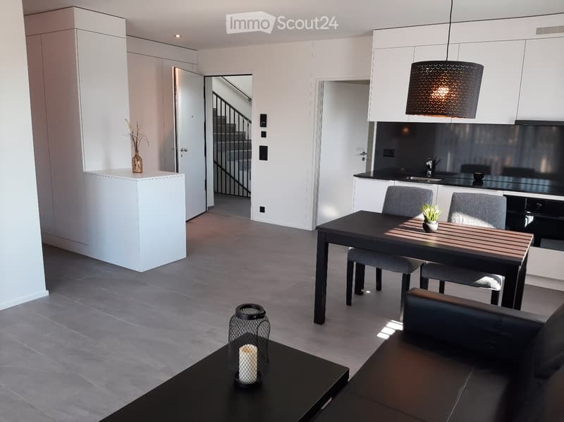 open plan living room with dining area, gray flooring, black dining table with chairs, black sofa, white cabinets, modern pendant lamp, staircase, coffee table with candle
