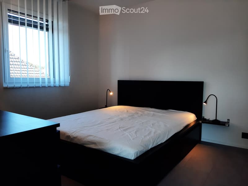Bedroom with a bed, desk, two lamps on the nightstands, and a window with blinds