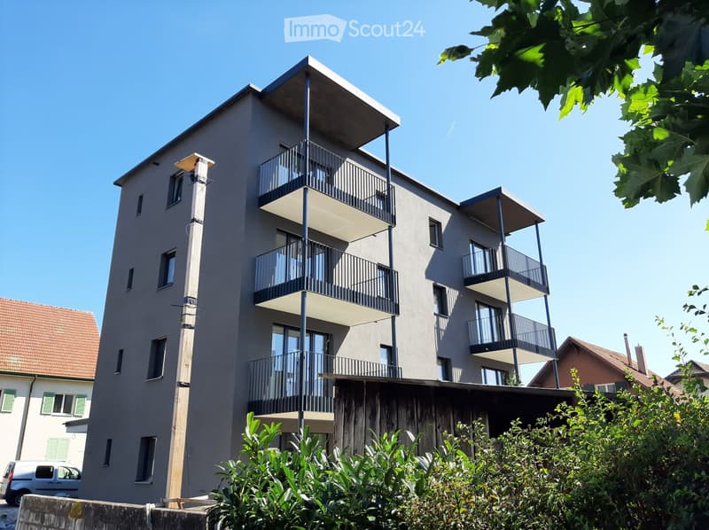 Modern apartment building, multiple floors, balconies, grey exterior, clear blue sky
