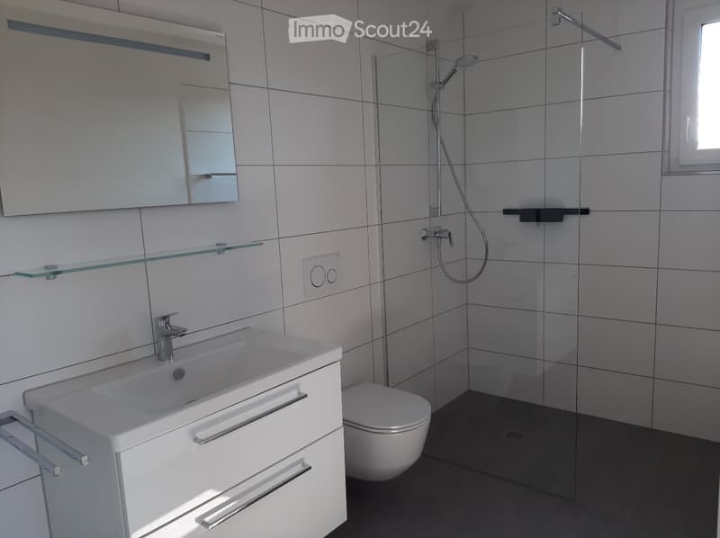 modern and spacious with white tiles, glass shower enclosure, silver faucet, white sink with drawers, recessed mirror, white toilet, and floor drain