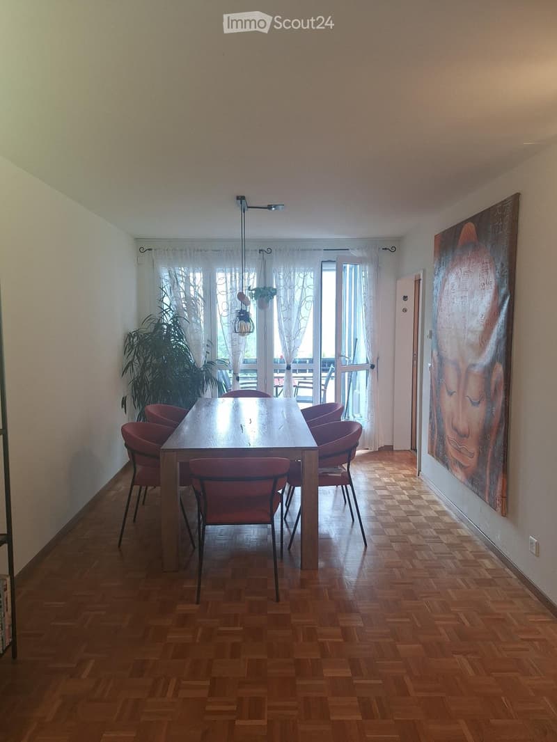 Dining room with wooden parquet flooring, a large wooden dining table surrounded by red chairs, a large painting on the wall, and a potted plant near the window.