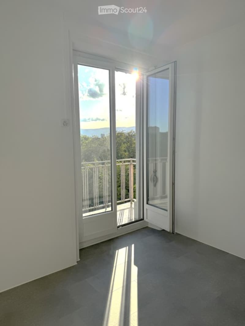 Empty room with large sliding glass doors leading to a balcony, white walls, and grey tiled floor.