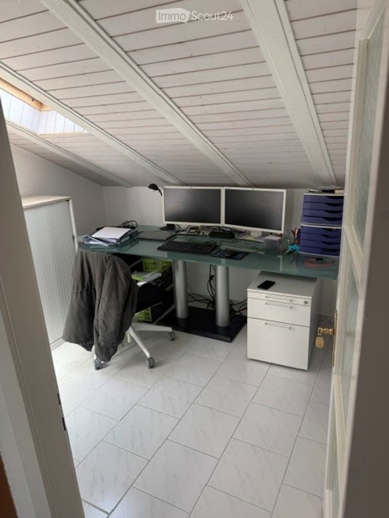Attic office space with slanted ceilings, white tiled floor, glass desk, two computer monitors, keyboard, mouse, chair, printer, and storage unit.