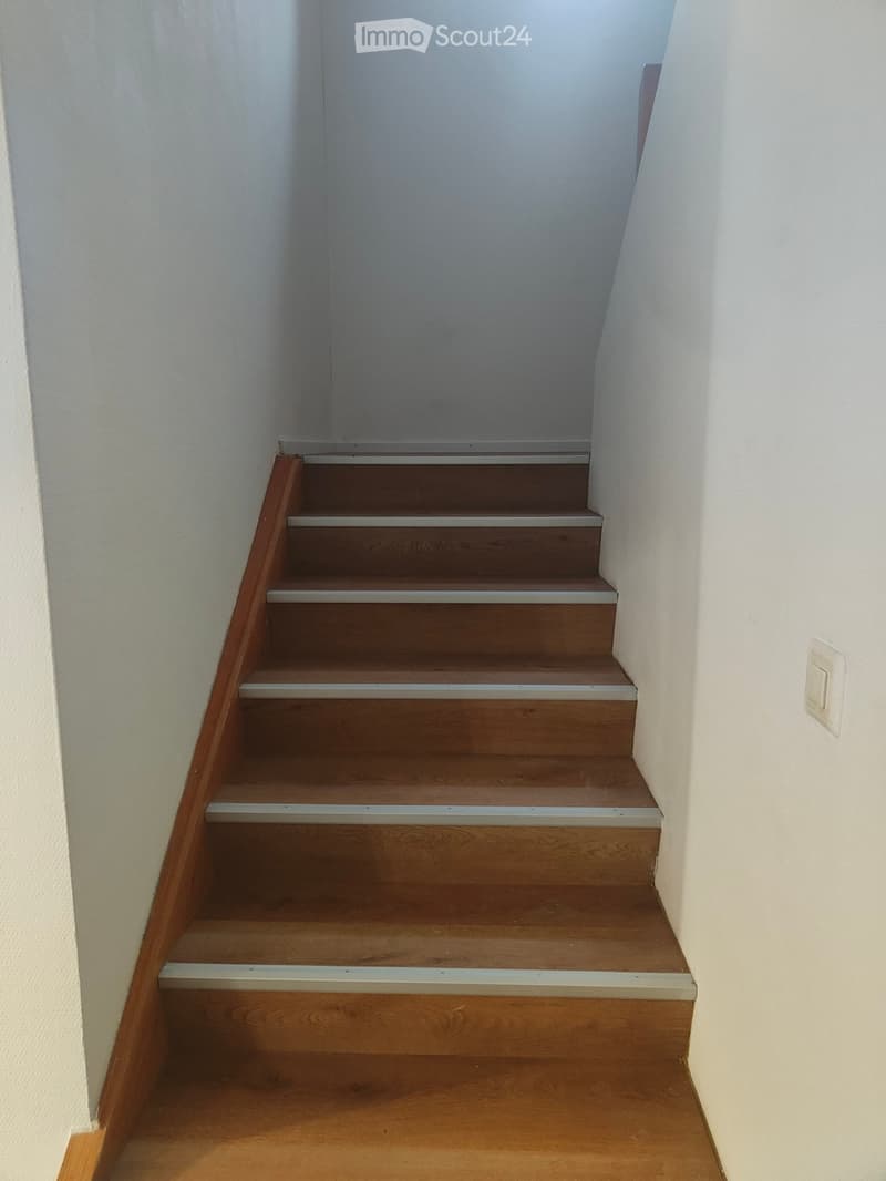 Wooden staircase with white walls and a light switch on the right side.