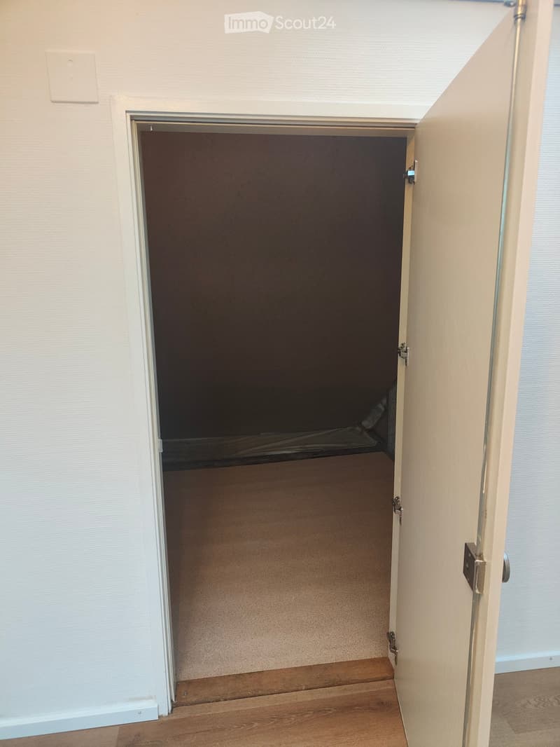 Open doorway leading to a dark room with wooden flooring and white walls.