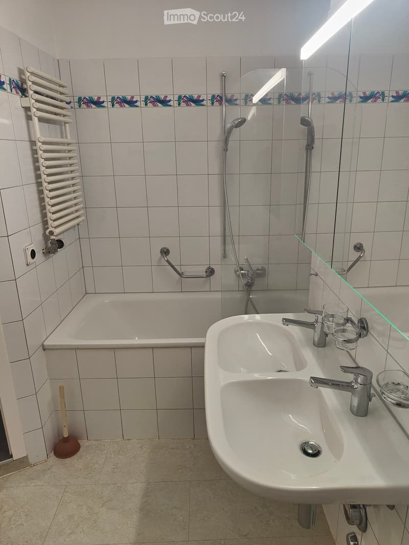 Bathroom with a bathtub, double sink, radiator, and a toilet brush on the floor.