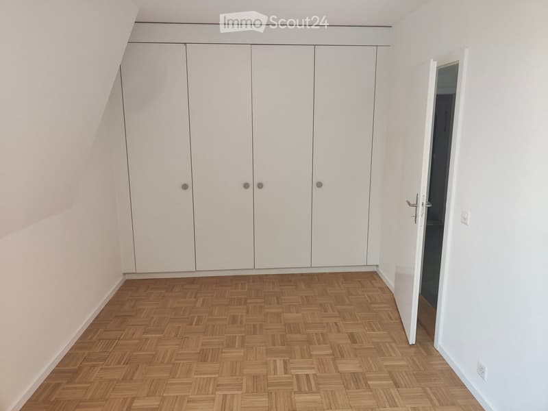 Empty room with white walls, wooden herringbone flooring, and built-in white closet units.