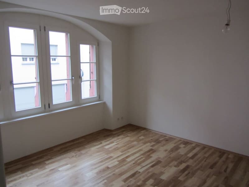 Empty room with wooden flooring and large windows, no furniture or equipment present.