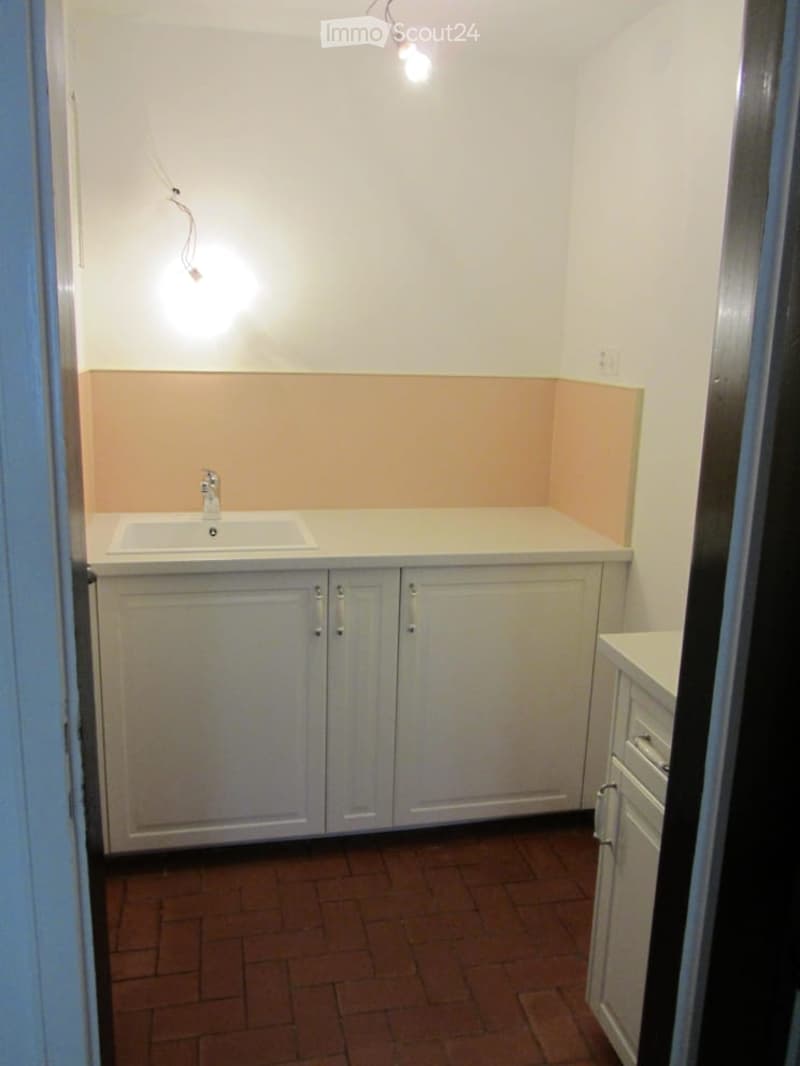 A small kitchen with white cabinets, a sink, and a tiled floor.