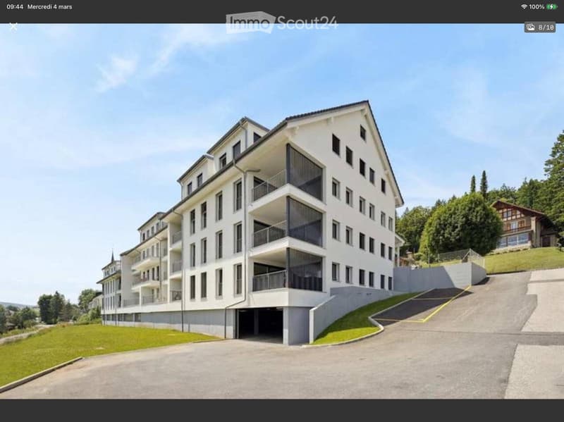 Modern apartment building with multiple floors, balconies, and a garage entrance.