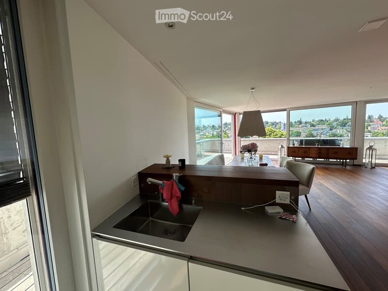 Modern kitchen with stainless steel sink, wooden countertop, and large windows offering a scenic view. Includes a dining area with a table and chairs.