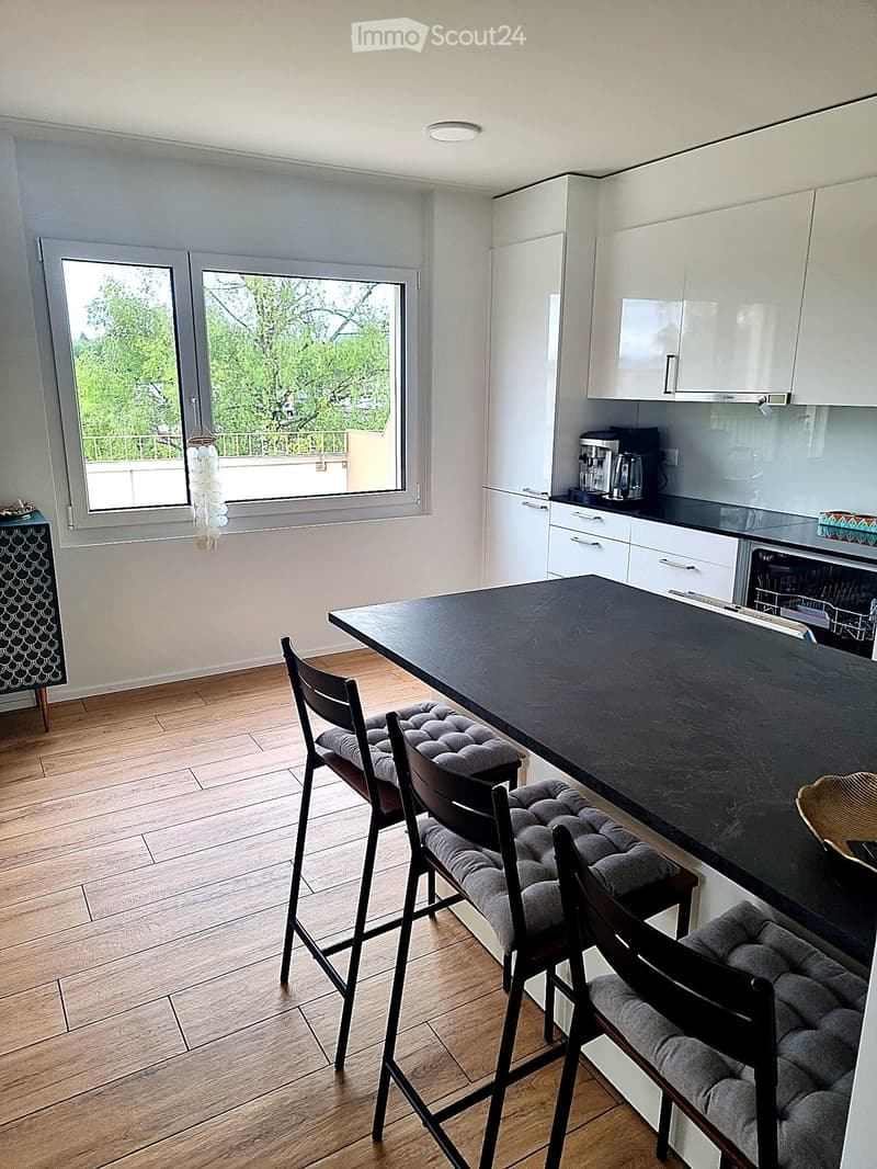 Modern kitchen with white cabinets, black countertop, and wooden flooring. Features a dining area with a black table and four upholstered chairs.