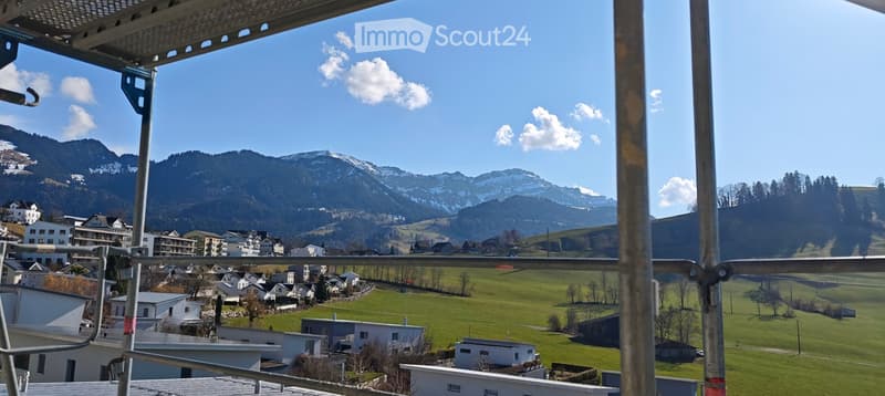 Aerial view of a town with many buildings and green fields, surrounded by mountains with snow
