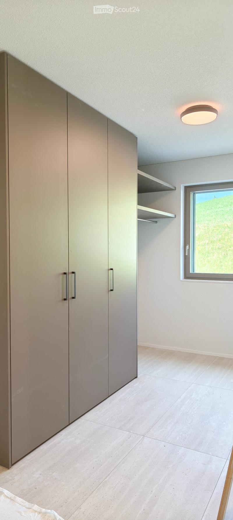 Empty room with light-colored tiled floor, built-in closet with mirrored doors, window with view, and recessed ceiling light.
