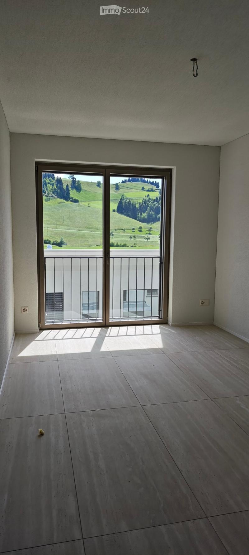 Empty room with large sliding glass doors leading to a balcony, tiled floor, and a scenic view of green hills and trees.
