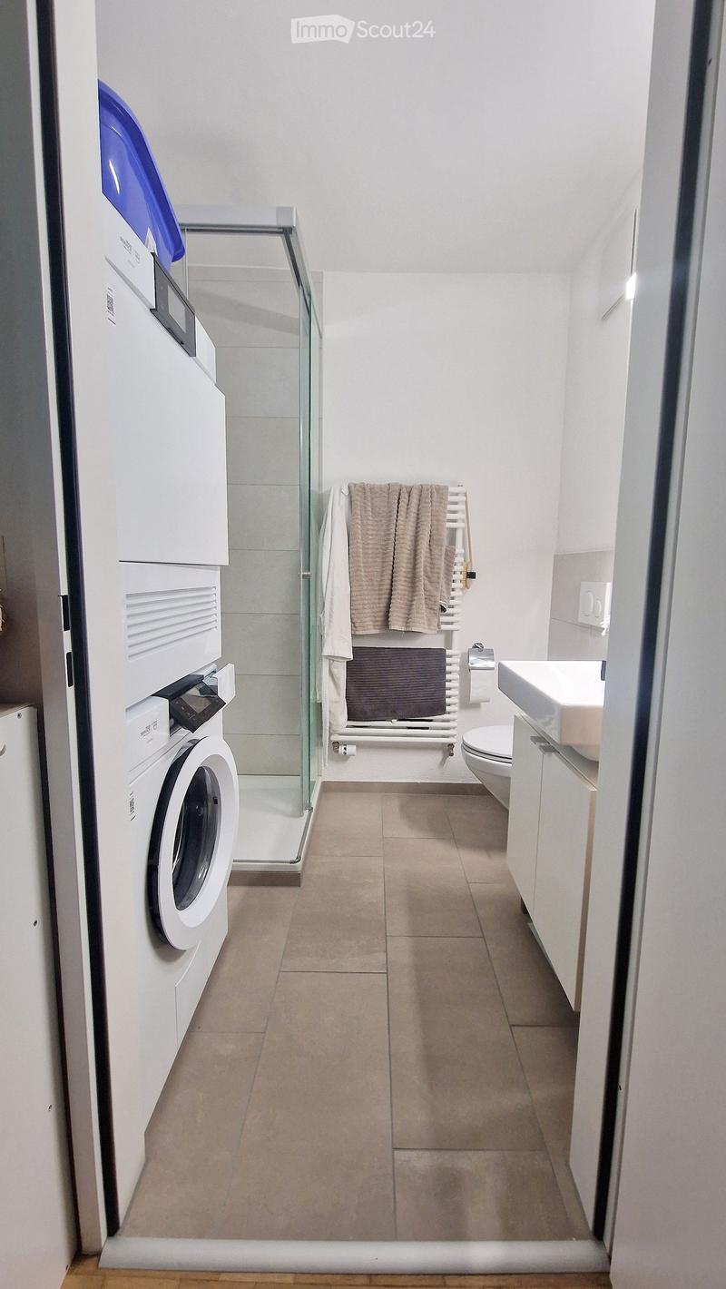 Modern bathroom with a washing machine, sink, toilet, radiator, and towels.