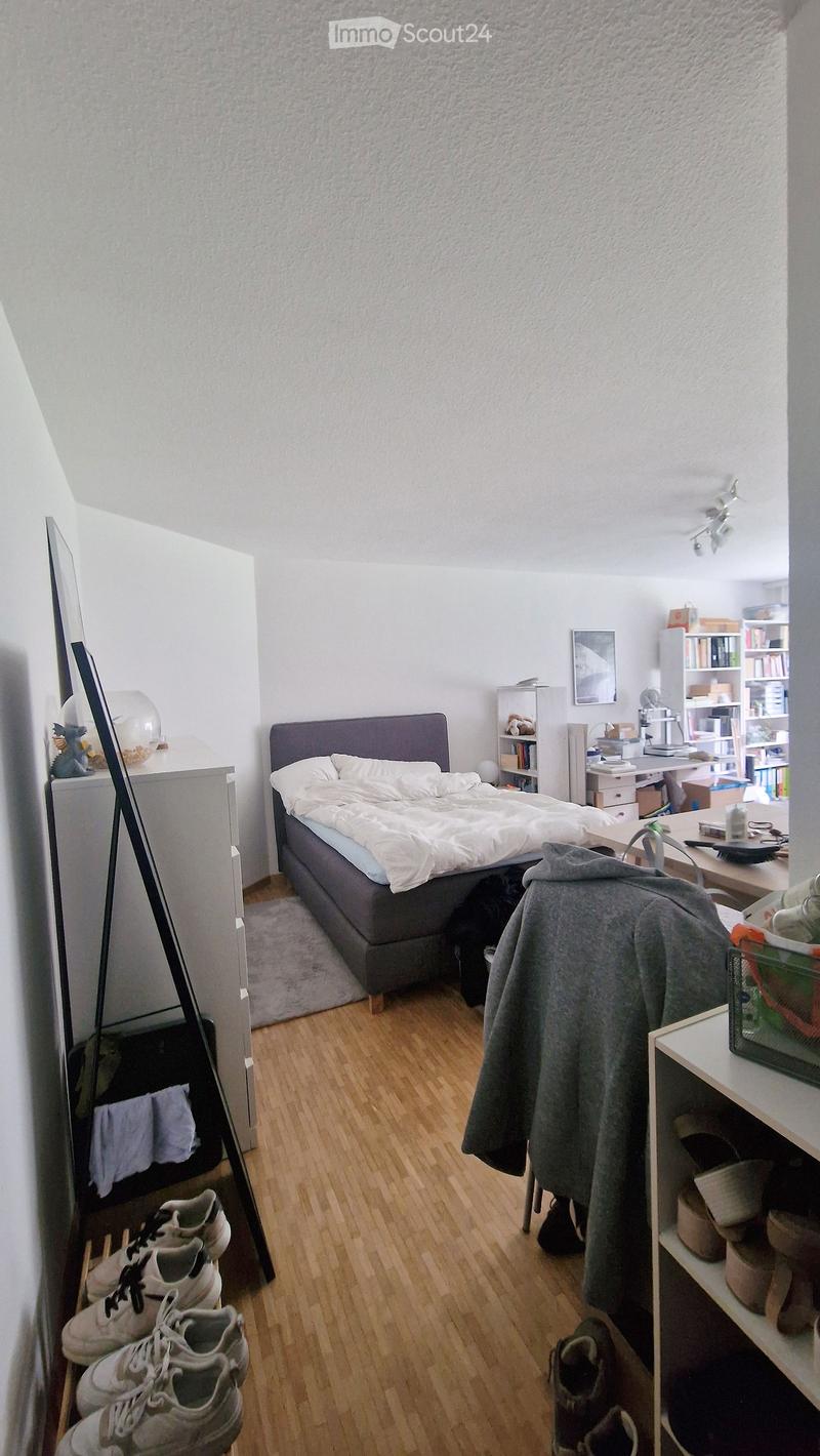 Cozy bedroom with a double bed, nightstand, bookshelf, desk, and a mirror. Wooden flooring and white walls.