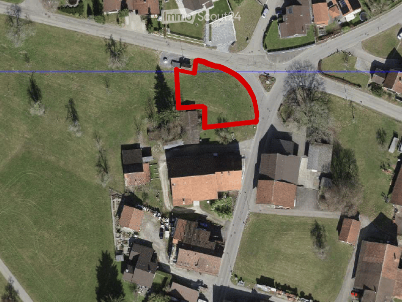 Aerial view of a residential area with multiple houses, roads, and green spaces. A red outline highlights a specific plot of land.
