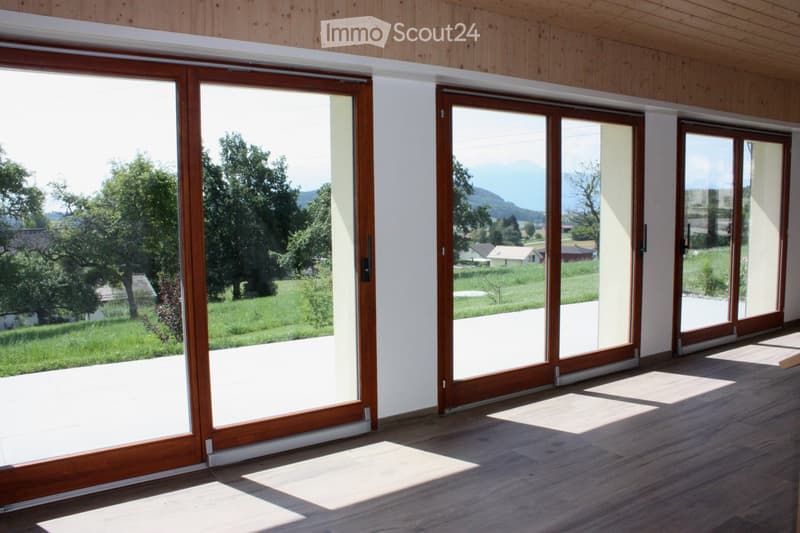 Empty room with wooden flooring and large sliding glass doors leading to a scenic outdoor view of a green field and trees.