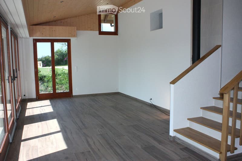 Empty room with wooden flooring, white walls, a staircase leading upwards, and large glass doors opening to a garden.