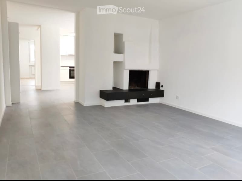 Empty living room with grey tiled floor, white walls, and a built-in fireplace with a black surround.