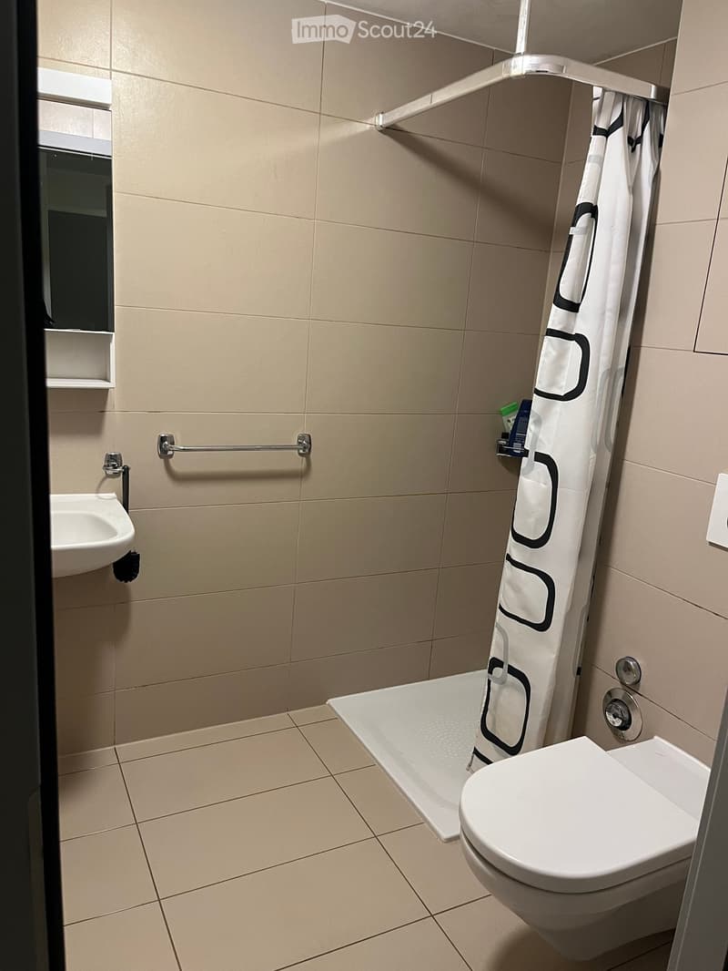Modern bathroom with beige tiles, a toilet, a sink, a bathtub, and a shower curtain with a black and white design.