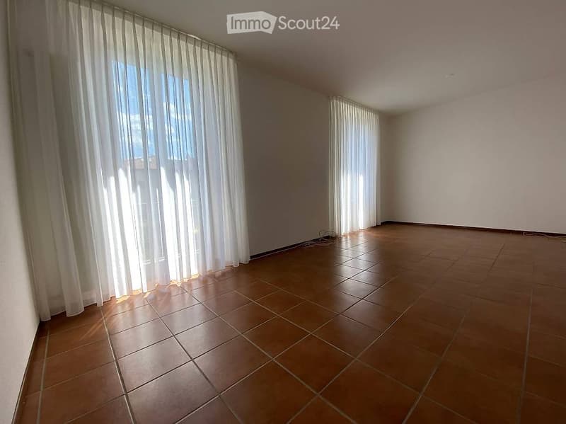 Empty room with tiled floor and large windows covered by white curtains. No furniture or equipment present.