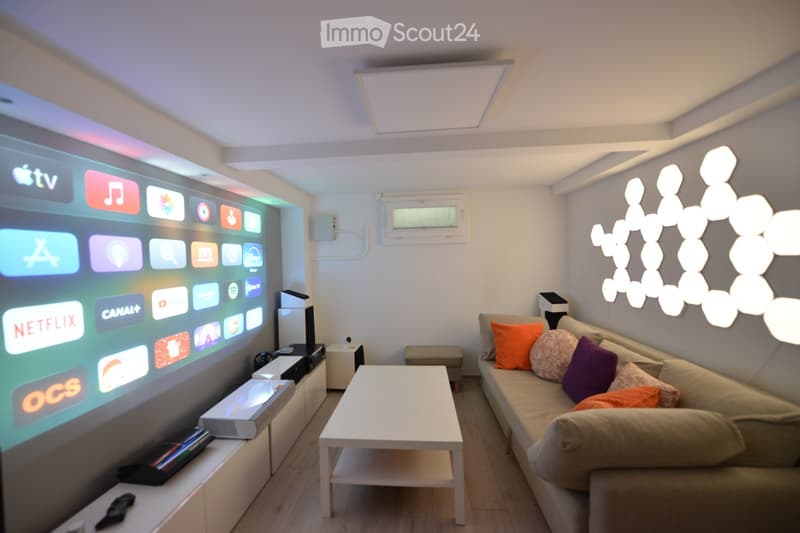 Modern living room with a large projector screen, a white coffee table, a beige sofa with colorful pillows, and a white entertainment center.