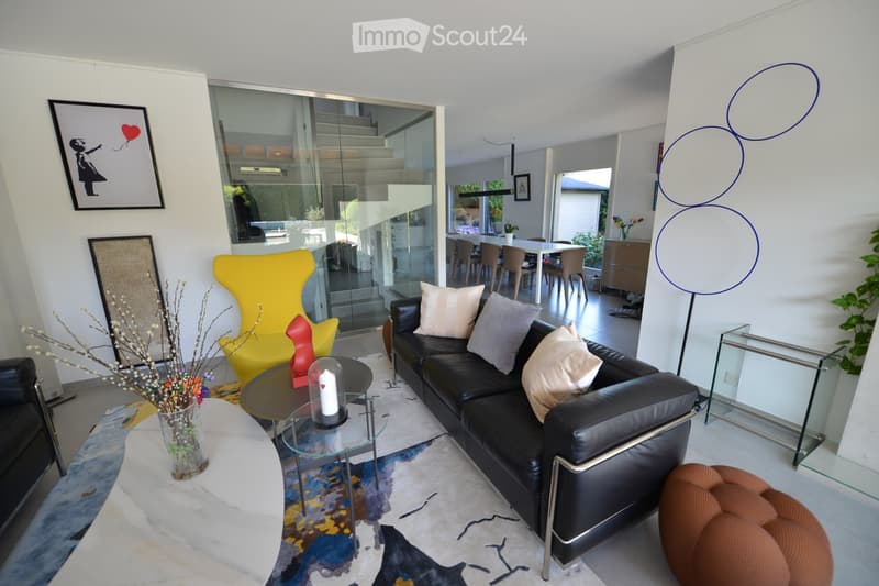 Modern living room with a black leather couch, glass tables, and a yellow chair. A colorful rug and decorative items add to the room's aesthetic.