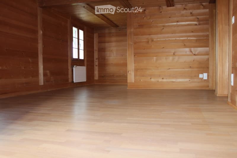 Empty wooden room with wooden walls, ceiling beams, and a window. No furniture or equipment present.