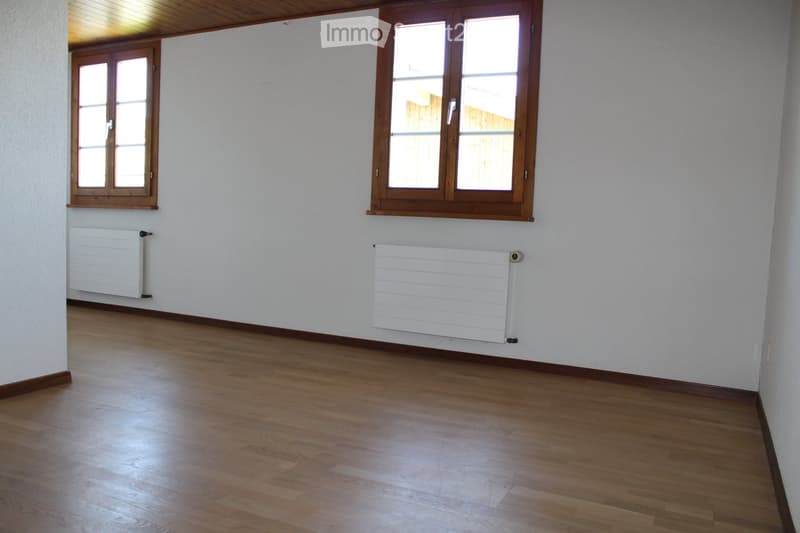 Empty room with wooden flooring, white walls, and two windows with wooden frames. Two white radiators are mounted on the walls.