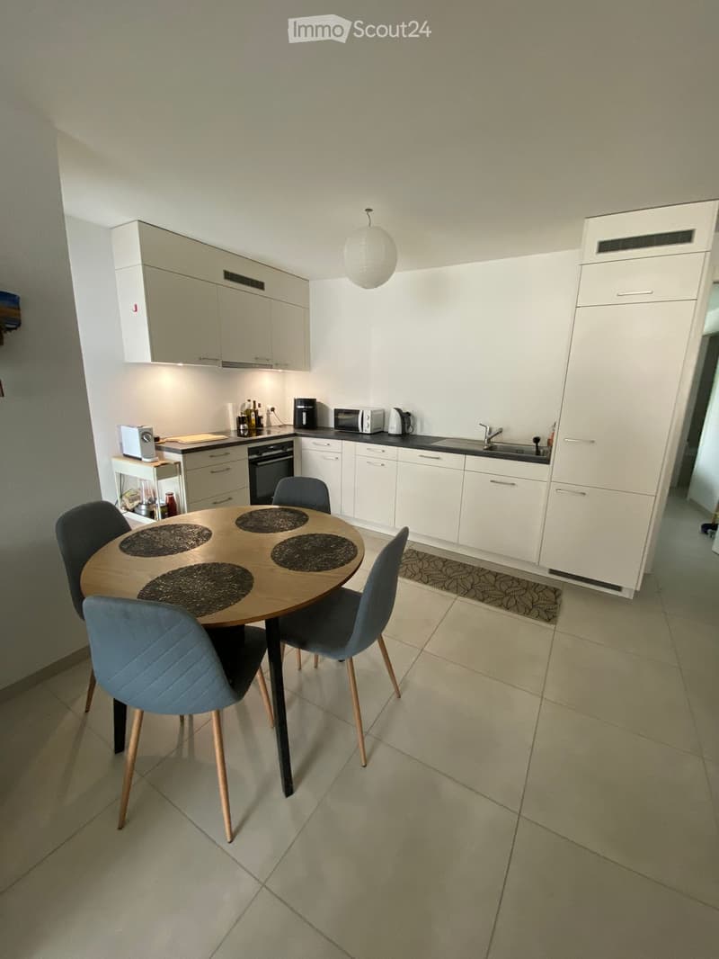 Modern kitchen with white cabinets, a dining table with four chairs, and various appliances including an oven, microwave, and coffee maker.