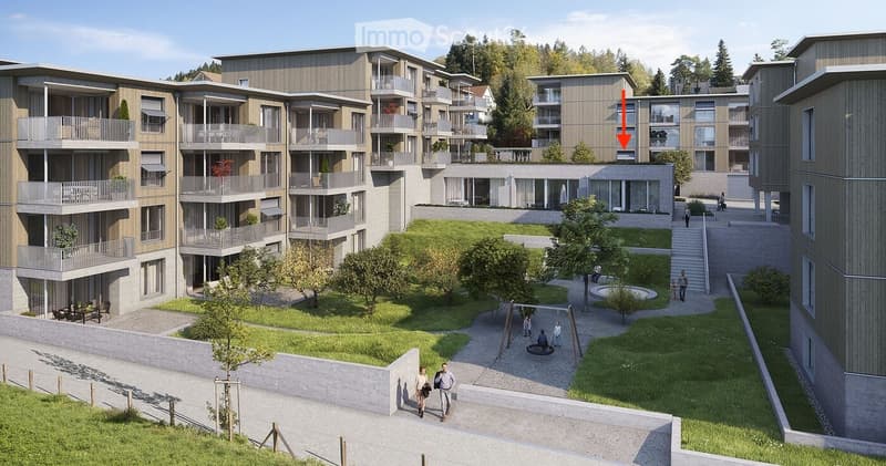 A modern multi-story residential complex with balconies, surrounded by greenery and pathways. The central courtyard features a small water feature, seating areas, and trees.