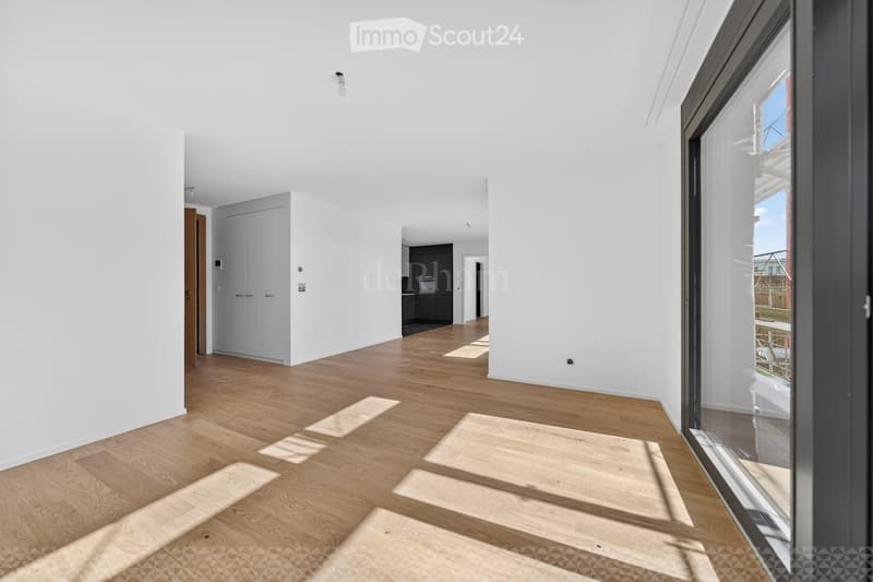 Empty hallway with light wooden flooring and white walls, featuring a large glass door leading to an outdoor area and a closed white cabinet.