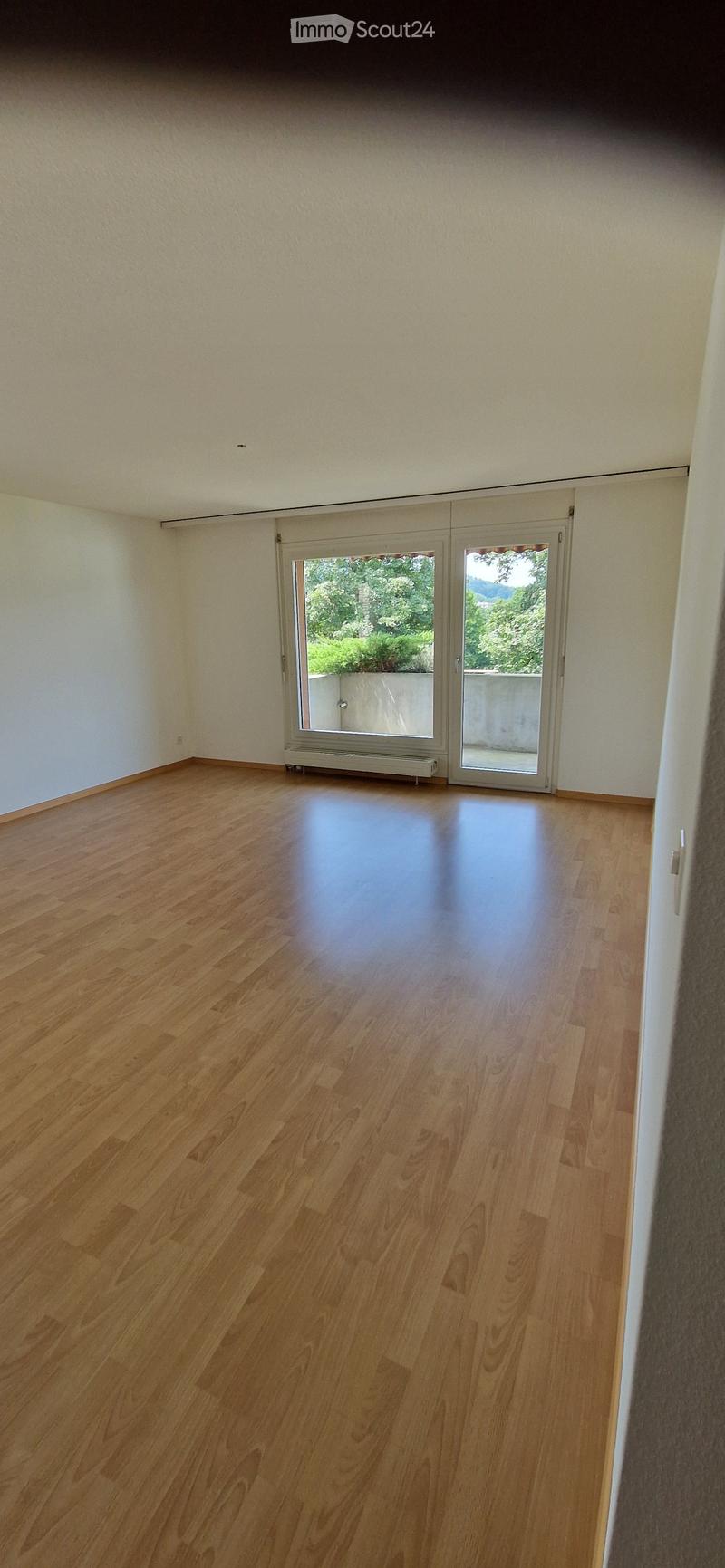 Empty room with wooden flooring, white walls, and large sliding glass doors leading to a balcony or outdoor area.