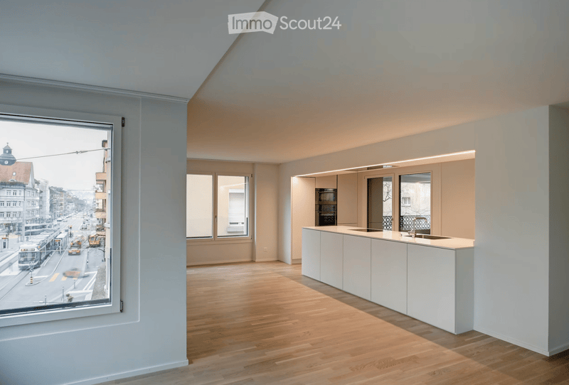 Modern, minimalist kitchen with a white island, sink, and built-in cabinets. The space features light wood flooring and large windows offering a city view.