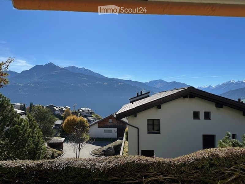Balcony overlooking a scenic mountain view with a house and surrounding landscape visible.