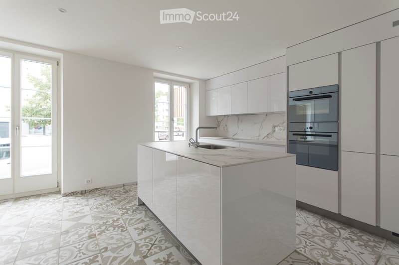 Modern kitchen with white cabinets, marble countertops, and a central island. Features a sink, faucet, and built-in oven.