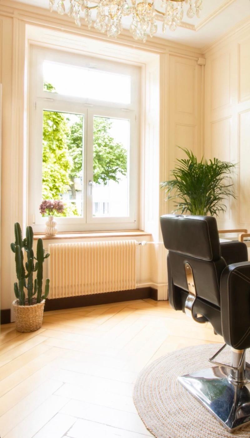 Bright room with large windows, a black leather chair, a cactus in a basket, a vase with flowers on the windowsill, and a radiator below the windows.
