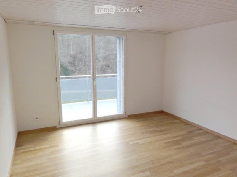 Empty room with light wooden flooring, white walls, and large sliding glass doors leading to a balcony.