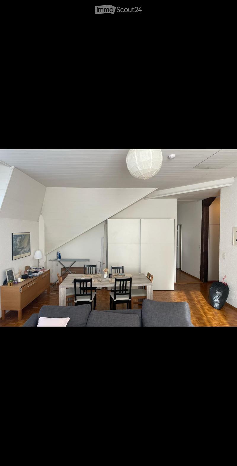 Bright living and dining area with wooden flooring, white walls, and modern furniture including a sofa, dining table, chairs, and a cabinet.