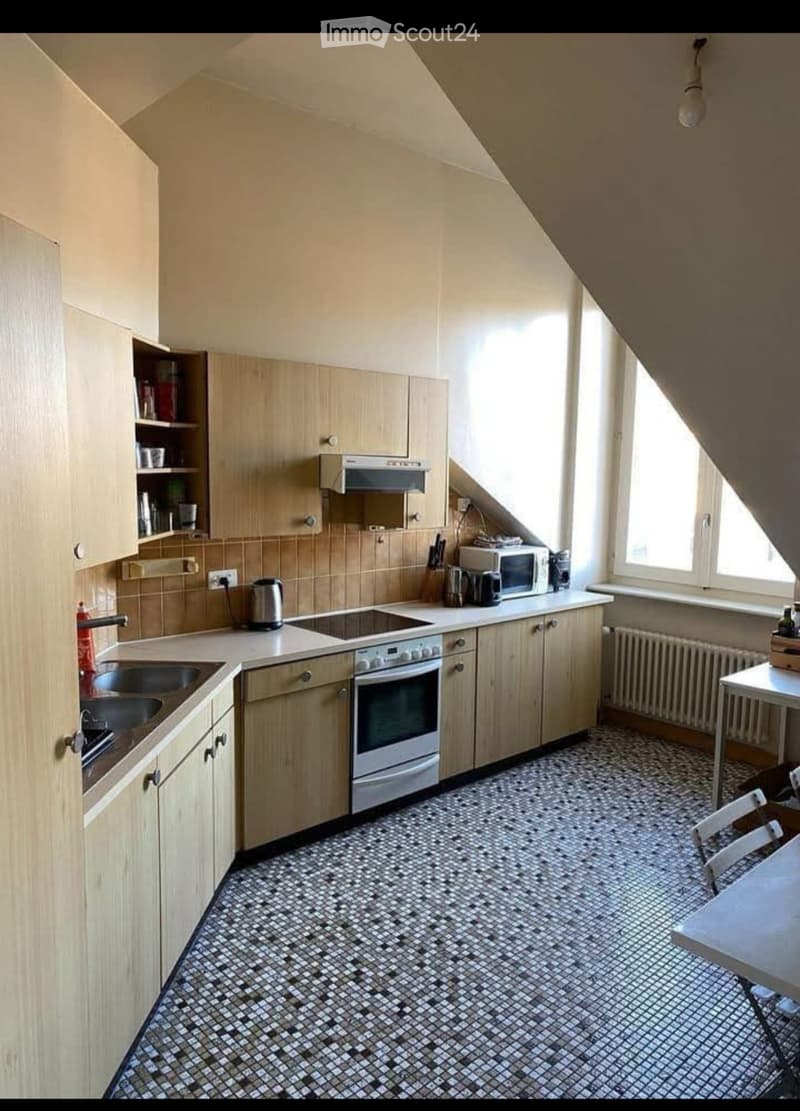 A compact kitchen with wooden cabinets, a tiled floor, and various appliances including a sink, oven, microwave, and a small table with chairs.